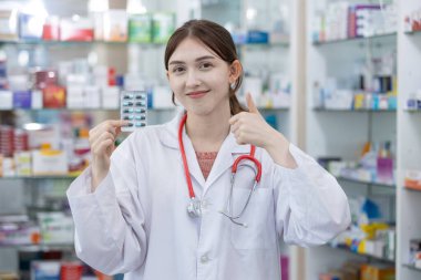 Eczanedeki raflarda su toplayan kadın eczacı gülümsüyor. Hastaya sunulan ilaç türü seçiliyor.