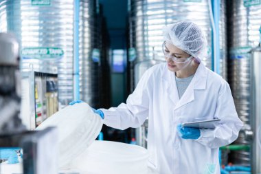 Kadın işçi, tüketicilere getirmek için plastik şişelere su doldurmadan önce büyük içme suyu tanklarının kalitesini kontrol ediyor. Fabrika üretim hattında su şişeleri. 