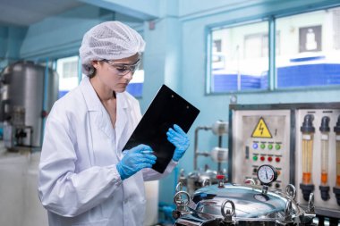 Kadın işçi QC tüketicilere getirmek için plastik şişelere su doldurma işleminden önce yüksek basınçlı içme suyu filtresi üretim hattında çalışıyor. Fabrikada su var..