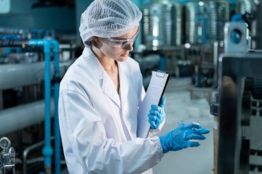 Kadın işçi QC tablet üretim hattını kullanarak yüksek basınçlı içme suyu filtresi ile suyu plastik şişelere doldurarak tüketicilere sunuyor. Fabrikada su var..