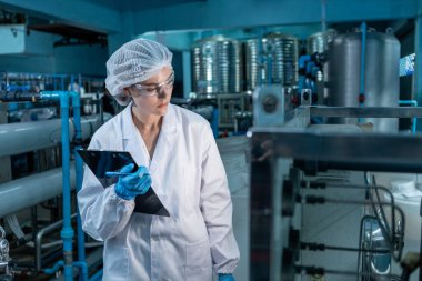 Kadın işçi QC tablet üretim hattını kullanarak yüksek basınçlı içme suyu filtresi ile suyu plastik şişelere doldurarak tüketicilere sunuyor. Fabrikada su var..