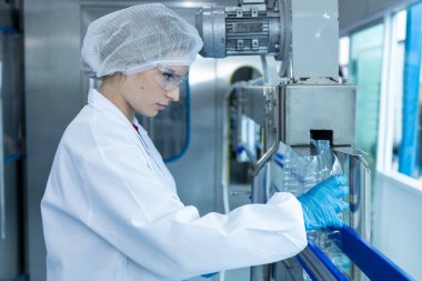 Plastik şişe hattı tutan kadın fabrika işçisi içecek suyu üretiyor. Kadın fabrika hattı şişe suyunu işlemek ve kontrol etmek için. Su içeceği üreten endüstriyel ürünler.