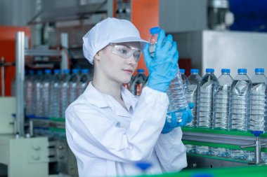 Kadın fabrika işçisi steril üniforma içecek suyu üretiyor. Şişe suyunu işlemek ve kontrol etmek için kadın fabrika hattı. Su içeceği üreten endüstriyel ürünler.