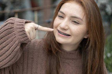 Kafkasyalı güzel bir kadının portresi. Sarı saçlı, süveter içinde Noel günü karla gülümseyen bir kadın. Diş telleriyle. Neşeli kız gülümse kameraya bakan dişlerini göster