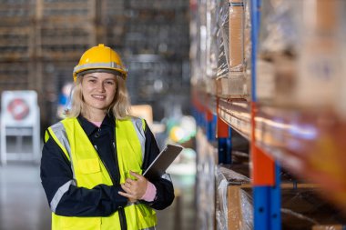 Depodaki raflarda dijital tablet kullanarak güvenlik üniforması ve başlık takan sarışın, profesyonel bir kadın. Kadın işçi fabrikada hisse senedi teftişi yapıyor..