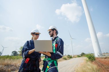 Team engineer wearing safety uniform holding laptop discussed plan about renewable energy at station energy power wind. technology protect environment reduce global warming problems.