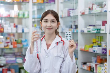 Eczanedeki raflarda su şişesi ve su toplayan eczacı. Hastaya sunulan ilaç türü seçiliyor.