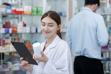 Kadın eczacılar, eczanedeki tablet aracılığıyla hastalar için internetten ilaç seçiyorlar. Uyuşturucu satıcısı, hastaya göndermeden önce ilaç şişesi tutarak bilgi almak için tablet kullanır.