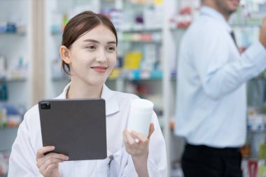Kadın eczacılar, eczanedeki tablet aracılığıyla hastalar için internetten ilaç seçiyorlar. Uyuşturucu satıcısı, hastaya göndermeden önce ilaç şişesi tutarak bilgi almak için tablet kullanır.