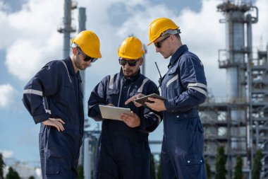 İstasyonda petrokimyayı rafine etmek için birlikte tablet kullanan bir mühendis. Teknisyen kalite petrol fabrikasını kontrol etti. Müfettiş rafineri binasının arka planında gaz bölgesinde duruyor..