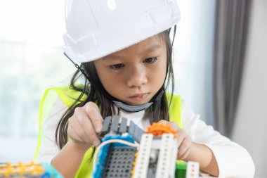 Kız çocuğu elektrikli oyuncaklar monte ederken beyaz şapka takıyor. Eğitim BTMM çocuk öğrencileri sınıfta. Robot montaj eğitimi, beyin gelişimi, elektrik geleceği mühendisliği..