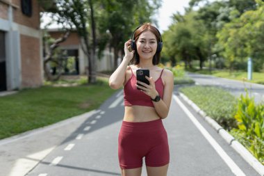 Genç ve güzel kadın spor kıyafetleri akıllı telefon kullanarak ve kulaklıkla müzik dinleyerek egzersiz yaparken mavi gökyüzü arka planında dinleniyor. fitness sağlıklı konsept.