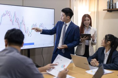 Çağdaş ofis ortamında mali raporları ve çizelgeleri tartışan bir grup profesyonel iş toplantısına katıldı. İstatistik ve şirket büyüme grafiklerinin beyin fırtınası ve analizi