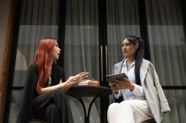 İki kadın tablet kullanarak oturmuş öğleden sonra dışarıda fikirleri tartışıyorlar. Sözlü ifadeleri anlamlı bir diyalog olduğunu gösteriyor. Kadın meslektaşım beyin fırtınası yapıyor..