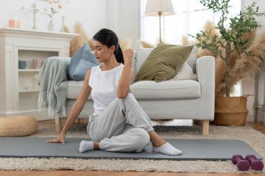Genç Asyalı kadın omuz gerdirerek yoga yapıyor oturma odasında yerde oturuyor. Rahatla, rahatla ve evde egzersiz yap. Etkinlik vücut hareketi egzersizleri.
