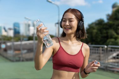 Spor yaparken su şişesinden su içen Asyalı genç bayan sporcu. Her gün susuz kalma. Sağlıklı, sağlıklı, sağlıklı, sağlıklı bir kadın. Su içmek iyi hissettirir..