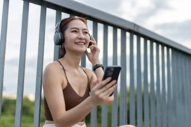 Genç, güzel kadınlar spor giyim akıllı telefonu ve kulaklıkla müzik dinlemek egzersiz sırasında şehir parkında dinlenir. Sağlıklı konsept.