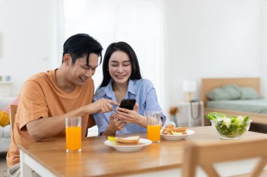 Çift birlikte gülerken yemek masasında portakal suyu ve kahvaltı malzemeleriyle akıllı telefonlara bakıyor..