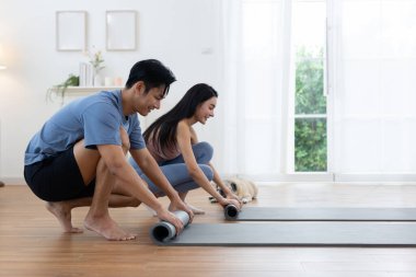 Çift, sabah antrenmanını tamamladıktan sonra yoga minderlerini yuvarlıyor. Köpekleri yakınlarda uzanıyor, parlak yaşam alanının rahat atmosferinin tadını çıkarıyorlar..