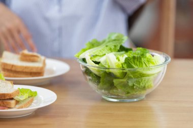 Taze salatayı kapalı mekan ortamında ahşap masaya koy. Çift sağlıklı kahvaltıyı sandviçle yiyor..