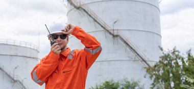 Turuncu tulumlu profesyonel mühendis ve telsiz telsizinden beyaz başlıklı adam ileri işaret ederken. Petrol petrokimya sanayii fabrikasında rafineride çalışıyorum..