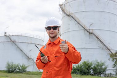 Turuncu tulumlu profesyonel mühendis ve telsiz telsizinden beyaz başlıklı adam ileri işaret ederken. Petrol petrokimya sanayii fabrikasında rafineride çalışıyorum..