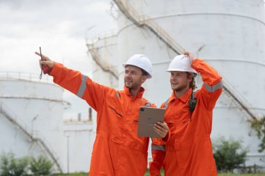 Petrokimya endüstrisi fabrikasının rafine edilmesi için endüstriyel depolama tanklarının yanında tablet kullanan güvenlik donanımı işçisi..