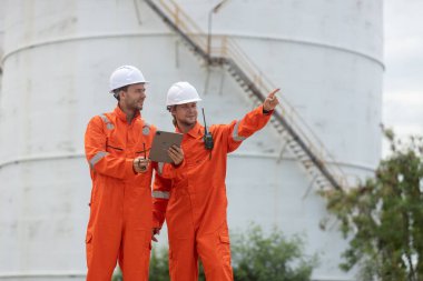 Petrokimya endüstrisi fabrikasının rafine edilmesi için endüstriyel depolama tanklarının yanında tablet kullanan güvenlik donanımı işçisi..