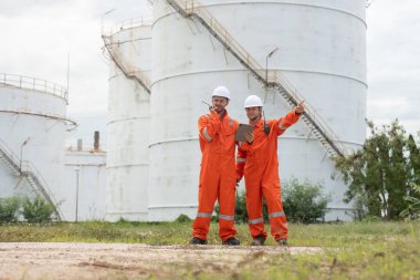 Petrokimya endüstrisi fabrikasının rafine edilmesi için endüstriyel depolama tanklarının yanında tablet kullanan güvenlik donanımı işçisi..