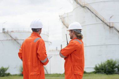Petrokimya endüstrisi fabrikasının rafine edilmesi için endüstriyel depolama tanklarının yanında tablet kullanan güvenlik donanımı işçisi..