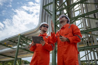 İnşaat alanında boru hattı projesini izleyen turuncu takım elbiseli ve beyaz kasklı iki işçi amiri. Endüstriyel tüp petrol petrokimyasında mühendis.