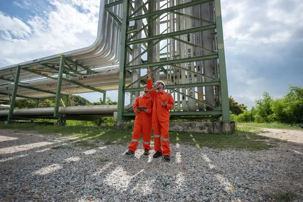 İnşaat alanında boru hattı projesini izleyen turuncu takım elbiseli ve beyaz kasklı iki işçi amiri. Endüstriyel tüp petrol petrokimyasında mühendis.