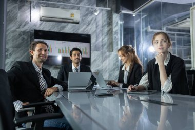 Çağdaş ofiste konferans masasında beyin fırtınası yapan bir grup profesyonel. Strateji planlaması için fikirleri paylaşıyor ve veri sunumlarını gözden geçiriyorlar.