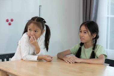İki genç kız kardeş iyi aydınlatılmış bir odada ahşap bir masada dikkatle konuşuyorlar. Pencerelerden gelen doğal ışık sıcak atmosferi güçlendiriyor ve davetkar bir alan yaratıyor..