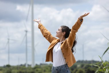 Kadınlar kolları açık dururlar, açık gökyüzü gününün altında rüzgâr türbinleriyle bezenmiş yeşil tarlalarda serin meltemi kucaklarlar. Gülüşü neşe ve özgürlüğü yansıtıyor..