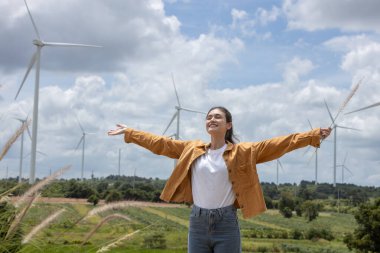 Kadınlar kolları açık dururlar, açık gökyüzü gününün altında rüzgâr türbinleriyle bezenmiş yeşil tarlalarda serin meltemi kucaklarlar. Gülüşü neşe ve özgürlüğü yansıtıyor..