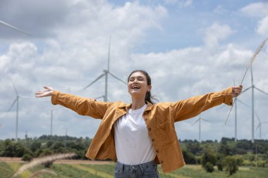 Kadınlar kolları açık dururlar, açık gökyüzü gününün altında rüzgâr türbinleriyle bezenmiş yeşil tarlalarda serin meltemi kucaklarlar. Gülüşü neşe ve özgürlüğü yansıtıyor..
