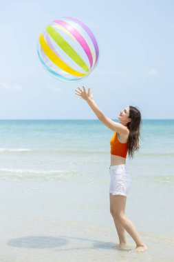 Güzel esmer kadınlar beyaz şort ve turuncu bluz giyip açık havada kumsala büyük, renkli bir plaj topu fırlatıyorlar. Rahatlama, iyi tatiller..