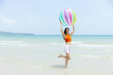 Güzel esmer kadınlar beyaz şort ve turuncu bluz giyip açık havada kumsala büyük, renkli bir plaj topu fırlatıyorlar. Rahatlama, iyi tatiller..