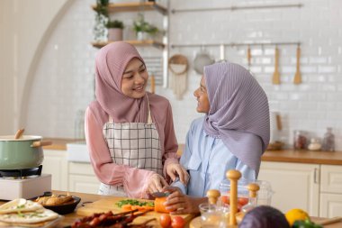 Günümüz mutfağında neşeli yemek pişirme tarzı, farklı yaşlardaki Müslüman kadın ve kız türbanları taze sebzeleri doğruyor ve renkli malzemeler ve mutfak eşyaları arasında yemek hazırlıyorlar..