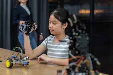 Kız, atölyede teknoloji ve robot bilimine odaklanmış el yapımı robotik el kaldırıyor. Öğrenci eğitim sapı, sınıfta robot el çalışması. Yenilik öğrenme elektronik sistem beceri eğitimi.
