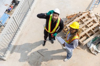 Güvenlik kaskı takan iki inşaat mühendisi ve inşaat alanındaki planları tartışan yansıtıcı yeleklerle takım çalışmasını ve planlamasını temsil ediyorlar. Yukarıdan görüntüle.