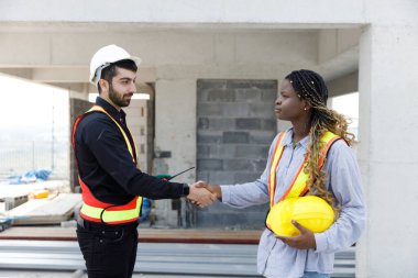 İnşaat işçileri inşaat alanında el sıkışıyor, takım çalışmasını, ortaklığı, güveni ve mühendislik ve inşaat alanlarındaki başarılı proje işbirliğini simgeliyor..