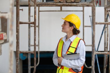 İnşaat alanında dijital tablet kullanan güvenlik kaskı ve yansıtıcı yelek giyen kadın inşaat mühendisi, teknoloji, proje yönetimi, güvenlik ve mühendislik çözümlerini temsil ediyor.