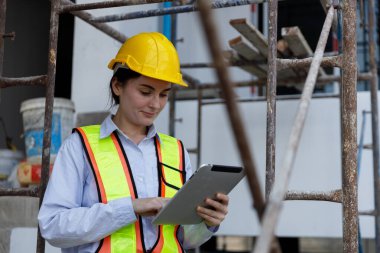 İnşaat alanında dijital tablet kullanan güvenlik kaskı ve yansıtıcı yelek giyen kadın inşaat mühendisi, teknoloji, proje yönetimi, güvenlik ve mühendislik çözümlerini temsil ediyor.