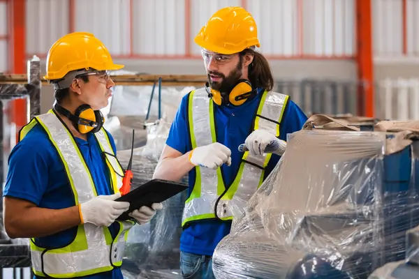 Güvenlik teçhizatındaki endüstri mühendisleri tablet ve telsiz kullanarak makine denetimini tartışıyor, fabrika ortamında iletişimi, hassasiyeti ve takım çalışmasını temsil ediyorlar..