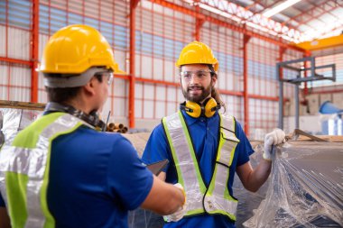 Fabrika ortamında bir tabletle tartışan güvenlik ekipmanı giyen iki sanayi işçisi, iletişim, takım çalışması, üretim süreci, işyeri güvenliği ve endüstriyel planlamayı temsil ediyorlar..