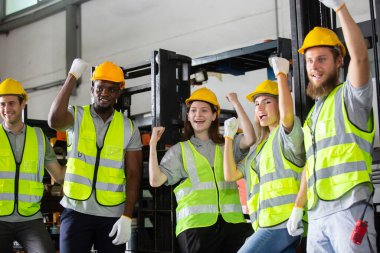 Güvenlik miğferleri ve yansıtıcı yelek giymiş mutlu inşaat işçileri başarıyı yükseltilmiş yumruklarla kutluyor, takım çalışmasını, motivasyonu, endüstriyel güvenliği ve iş yerinde pozitif işbirliğini simgeliyor.