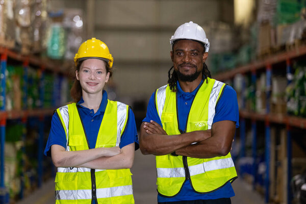 Портрет уверенных складских рабочих, стоящих вместе с скрещенными руками, в защитных шлемах и синей форме. Командная работа, профессионализм и безопасность на промышленных рабочих местах.