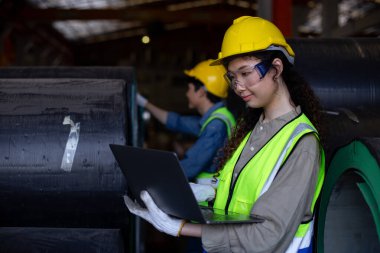 Kadın mühendis, metal levha fabrikası deposunda dizüstü bilgisayardaki verileri inceler, üretim izleme, envanter izleme ve endüstriyel iş akışı verimliliğine odaklanır..